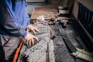Ruky mechanika, ktorý opravuje časti batérie elektromobilu na stole v dielni