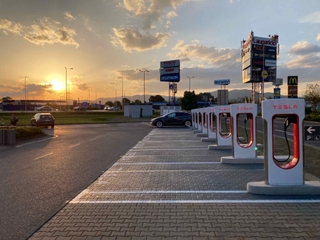 Supercharger Trenčín pri západe slnka. Pohľad na parkovisko bez áut s jednou Teslou na nabíjačke.